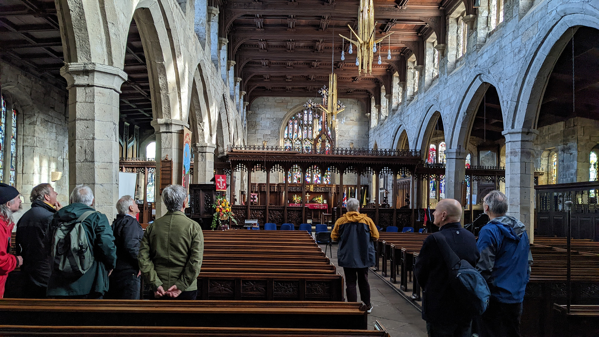 A photograph take during Stephen Marland's urban roam around Middleton. The image shows a group of 15–20 people inside a church. The people stand among the pews and look up at the architecture of the building.