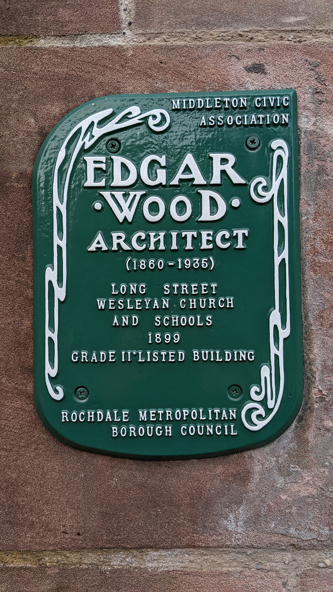 A photograph take during Stephen Marland's urban roam around Middleton. The image shows a decorative green plaque on the side of a building. The plaque commemorates architect Edgar Wood, who designed many of the buildings the tour group explored during the walk.