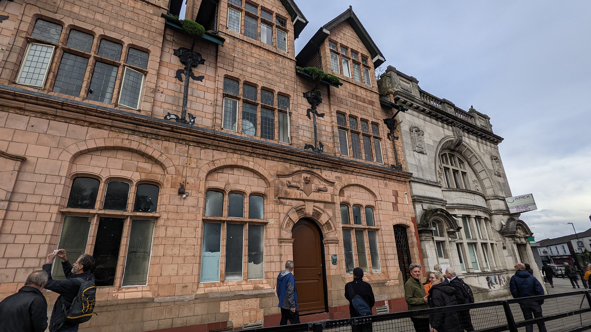 A photograph take during Stephen Marland's urban roam around Middleton. The image shows a group of people looking up ad taking photographs of a large brick building in Middleton.