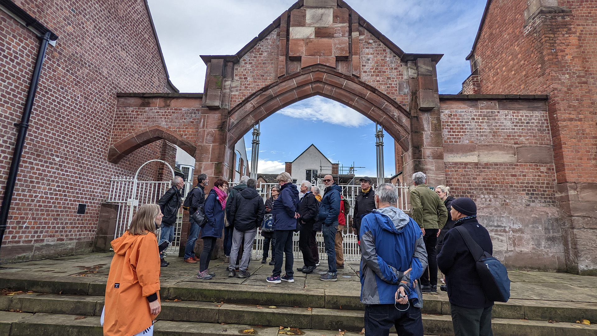 A photograph take during Stephen Marland's urban roam around Middleton. The image shows a group of people standing on steps leading up to an architecturally interesting red brick archway.